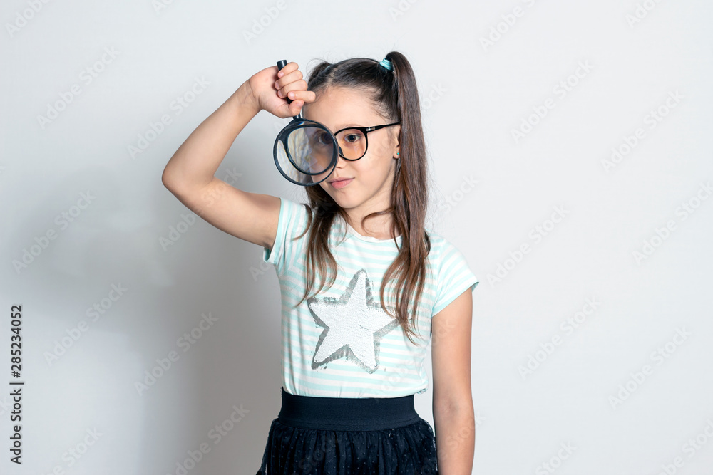 A little girl looks through a magnifying glass. The child plays detective A little girl looks through a magnifying glass. The child plays detective