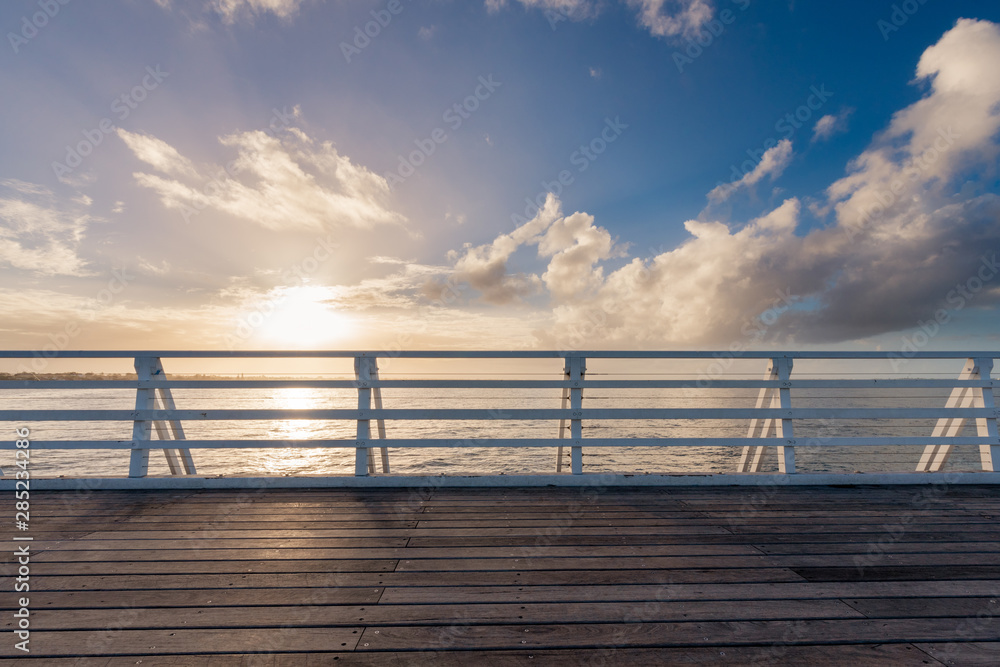A shot of the railings on a jetty walkway. The sun starts to make its way down over the horizon and casts beautiful yellow colours across the clouds in Brisbane, Queensland, Australia