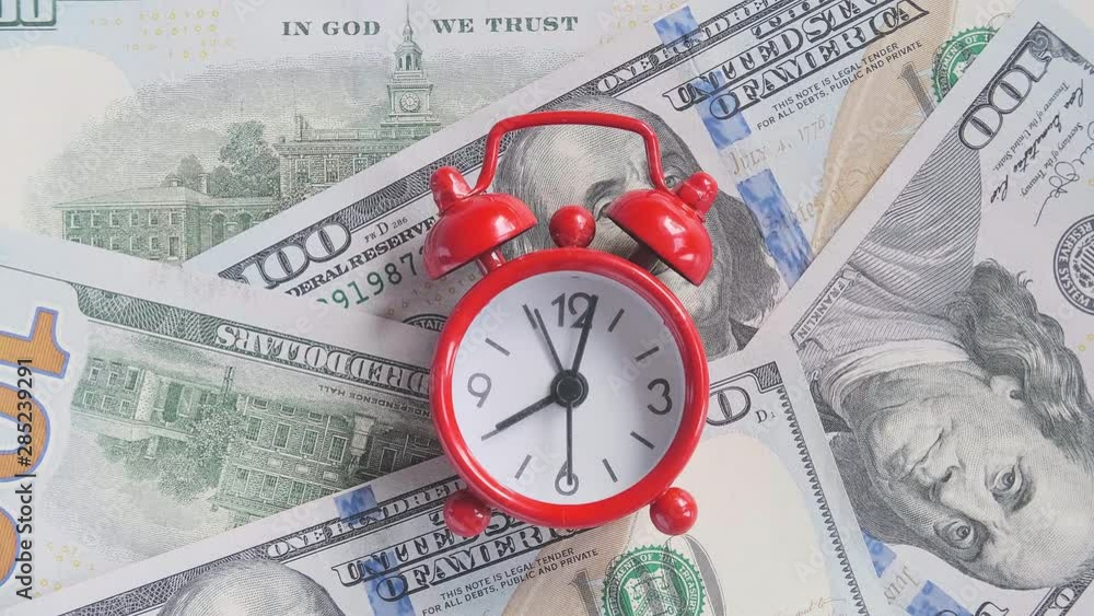 Red alarm clock walking ticking on the background of American hundreds dollar bills, closeup. Concept Time is money, Timelapse. Red alarm clock walking ticking on the background of American hundreds dollar bills, closeup. Concept Time is money, Timelapse.