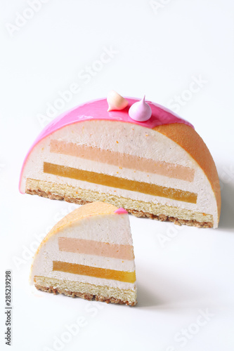Contemporary Dome Mousse Cake with pink grapefruit, orange and cream cheese mousse, covered with velvet spray and pink mirror glaze, on white background.