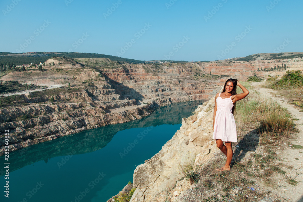 Naklejka premium beautiful woman with long hair sitting on a cliff by the lake