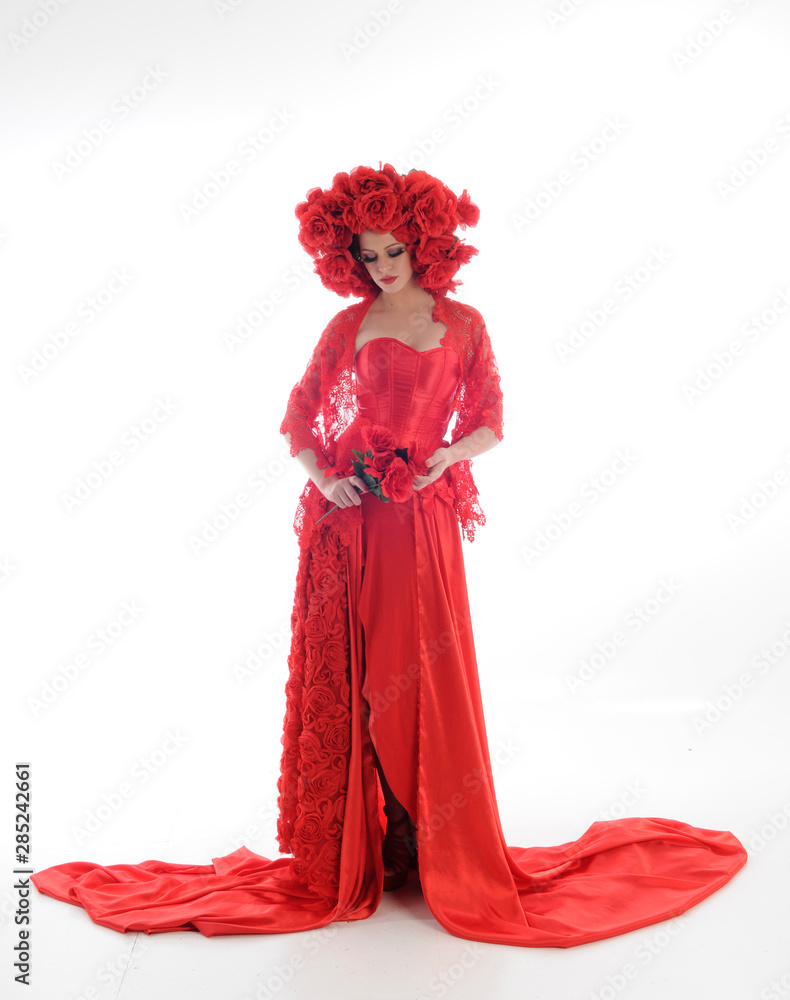 full length portrait of girl wearing long red silk gown and flower headdress. standing pose on white studio background.