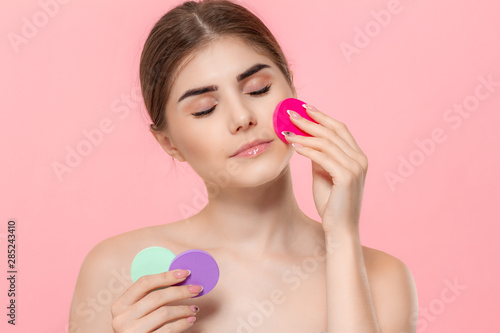 Beautiful model holds cotton sponges of different colors close to face.