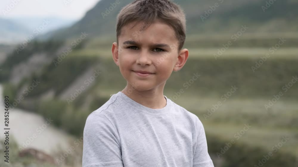 Portrait. Little tourist boy in a gray T-shirt looks at the camera on a background of mountains and a river Portrait. Little tourist boy in a gray T-shirt looks at the camera on a background of mountains and a river