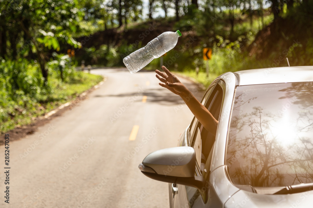 Male driver throwing away plastic bottle from car window on the road