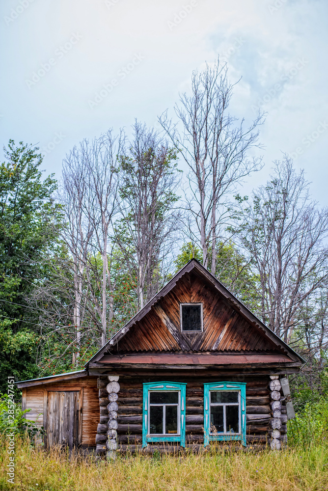 Old wooden house on the background of bare trees and cloudy sky