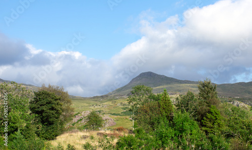 Wales, the Snowdonia national park. The rolling hills before the high peaks. A summers day. Fair weather cloud and blue skies. Shadows on the rugged green hill sides. Open air, health and nature.