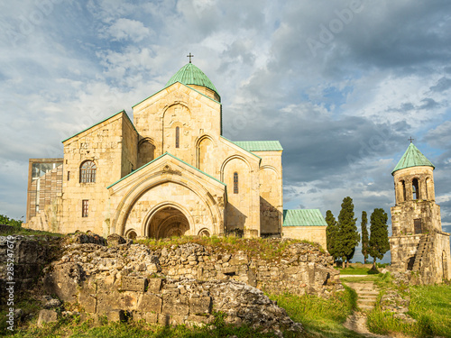 Stone ruined walls and majestic Bagrati cathedral behind them, illuminated by the evening sun. The church is a distinct landmark in the scenery of central Kutaisi,