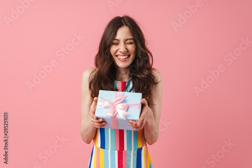 Pretty cheerful smiling positive cute woman posing isolated over pink wall background holding present gift box.