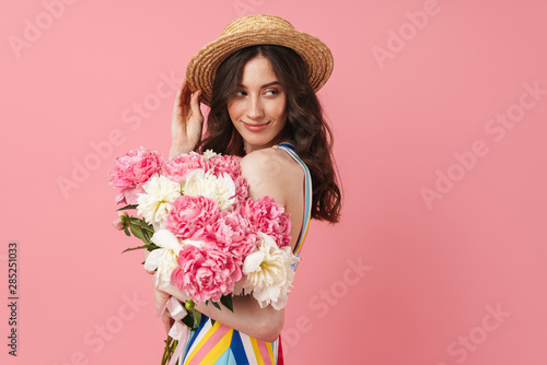Happy cheery smiling young cute woman posing isolated over pink wall background holding flowers.
