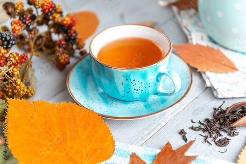 composition still life of a mug with hot leaf tea with berries and autumn leaves on a wooden surface