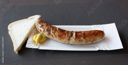 Rostbratwurst vom Grill, auf einem Pappdeckel mit Senf und einer halben Scheibe Toastbrot.