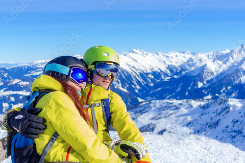 Happy young couple sitting on a bench a snowy slope and looking at a landscape of snowy Alps.