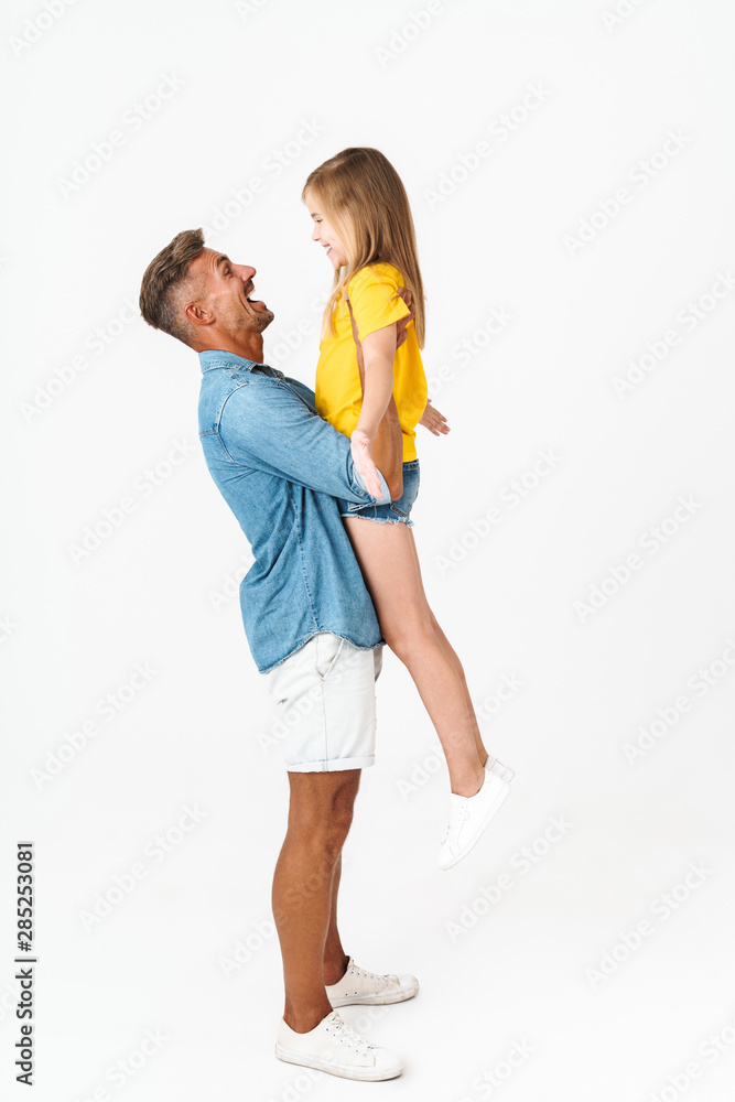 Full length photo of young caucasian father smiling and holding his daughter in arms Full length photo of young caucasian father smiling and holding his daughter in arms