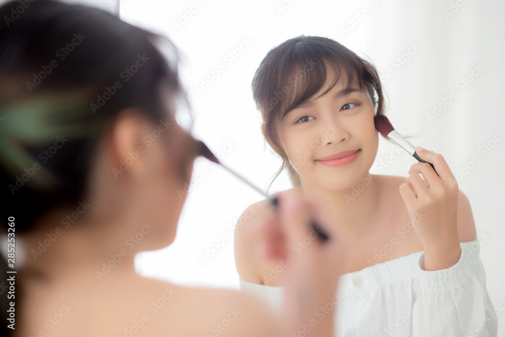 Beauty portrait young asian woman smile with face looking mirror applying makeup with brush cheek in the bedroom, beautiful of girl holding blusher, skin care and cosmetic concept. Beauty portrait young asian woman smile with face looking mirror applying makeup with brush cheek in the bedroom, beautiful of girl holding blusher, skin care and cosmetic concept.