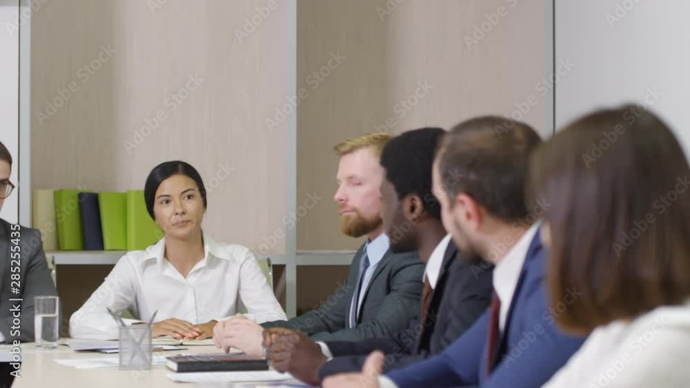Panning medium shot of six multiethnic male and female corporate employees in business attire sitting together at planning meeting and discussing new ideas and strategies Panning medium shot of six multiethnic male and female corporate employees in business attire sitting together at planning meeting and discussing new ideas and strategies