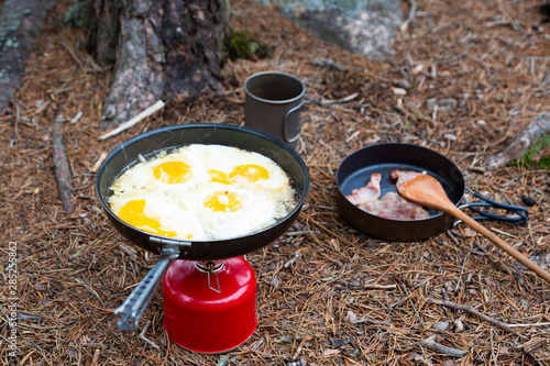 Breakfast, bacon and fried egg on a titanium plate. Tourism in the summer forest. Camping concept.