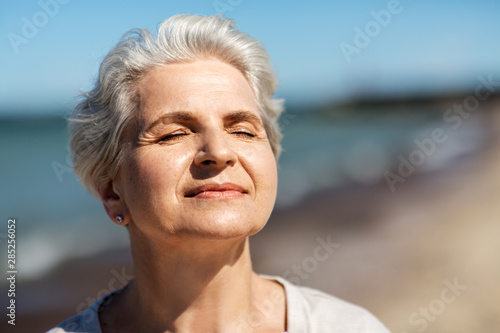 people and leisure concept - portrait of happy senior woman enjoying sun on beach