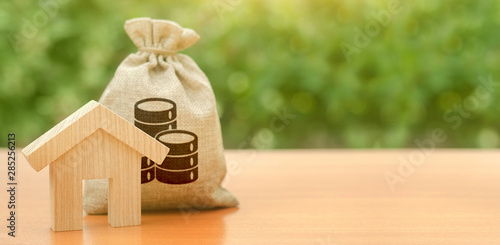 Wooden house figurine and a money bag. Family budget, control and reduction of expenses. subsidized funds. Mortgage loan for purchase housing, construction or modernization. Tax, building maintenance.
