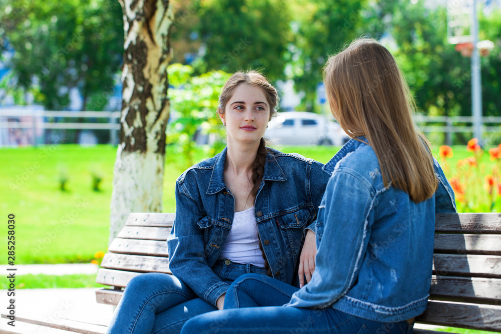 Two beautiful girlfriends are talking in a park sitting on a bench Two beautiful girlfriends are talking in a park sitting on a bench