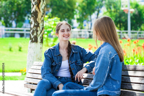Two beautiful girlfriends are talking in a park sitting on a bench