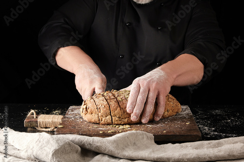 baker in black uniform cuts a knife into slices of rye bread