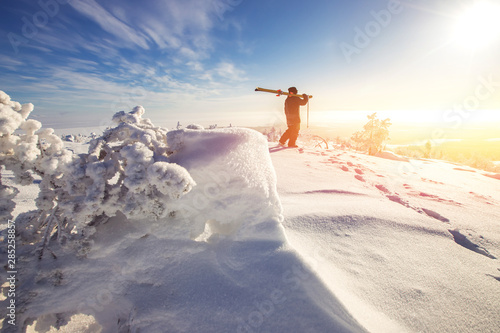 Tableau sur toile Man skier stands with ski on mountain top on sunrise backdrop