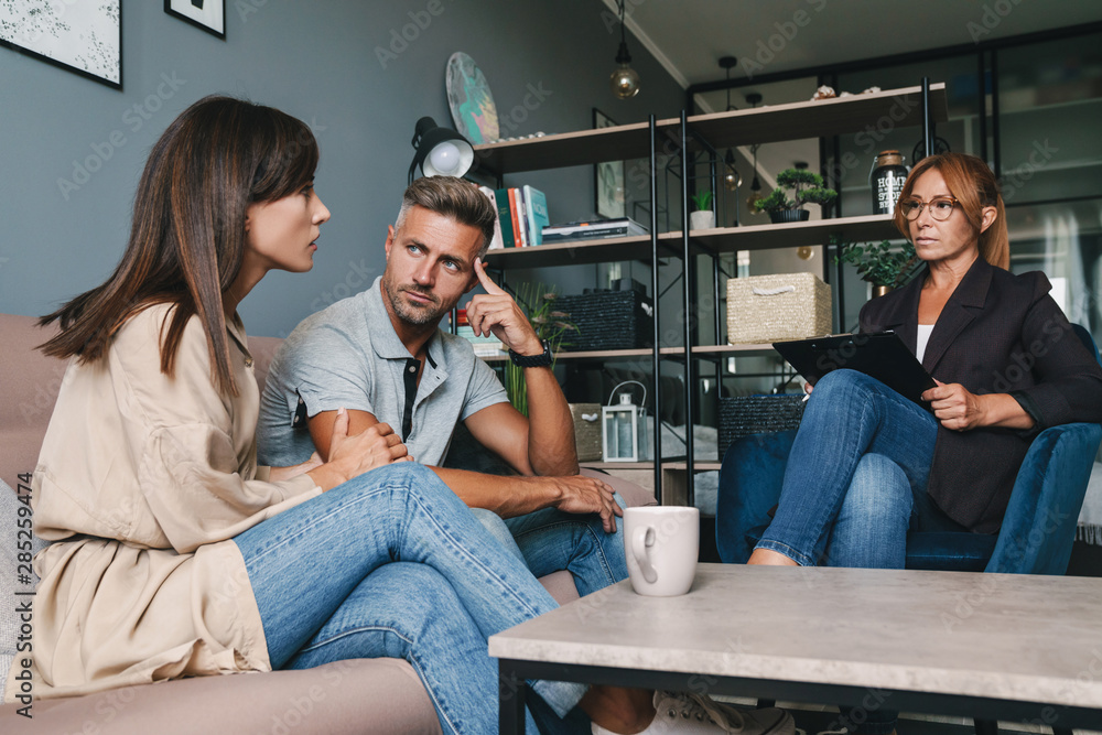 Photo of caucasian focused couple having conversation with psychologist on therapy session in room Photo of caucasian focused couple having conversation with psychologist on therapy session in room