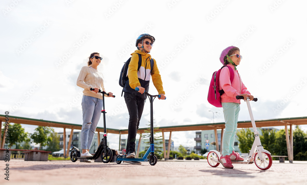 education, school and family concept - happy daughter, son and mother riding scooters outdoors education, school and family concept - happy daughter, son and mother riding scooters outdoors