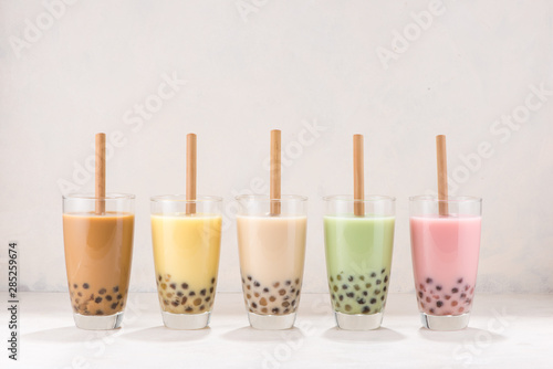 Row of fresh boba bubble tea glasses with straw on white background.
