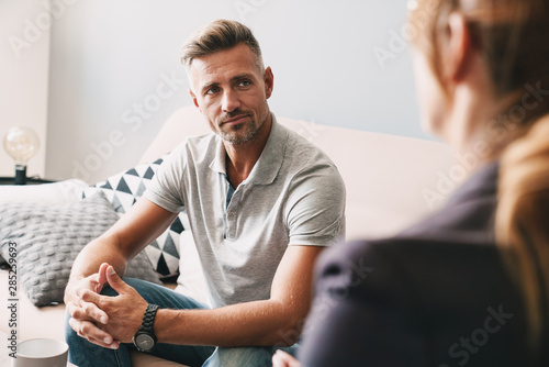 Obraz na płótnie Photo of confident focused man having conversation with psychologist in room