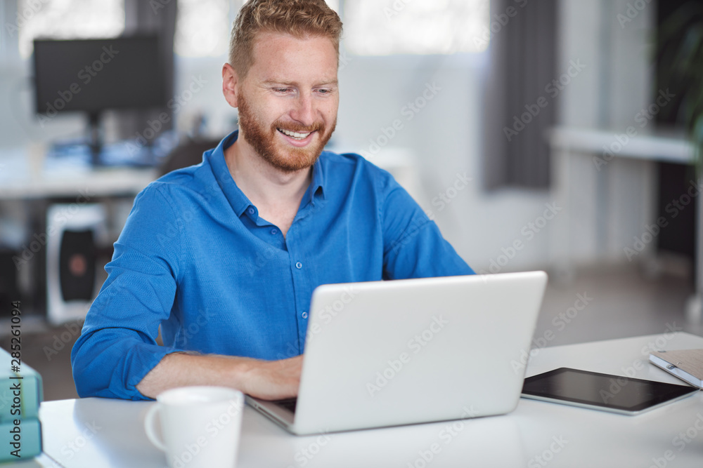 Young Caucasian employee sitting in office and typing on laptop. Start up business concept. Young Caucasian employee sitting in office and typing on laptop. Start up business concept.