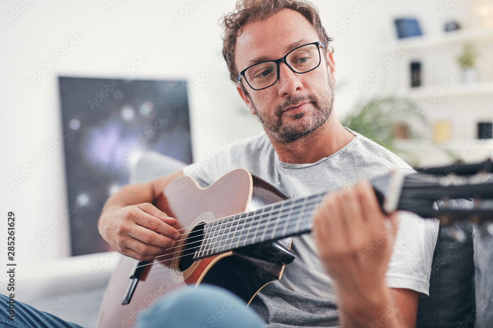 Man playing acoustic guitar in the living room. - obrazy, fototapety, plakaty 