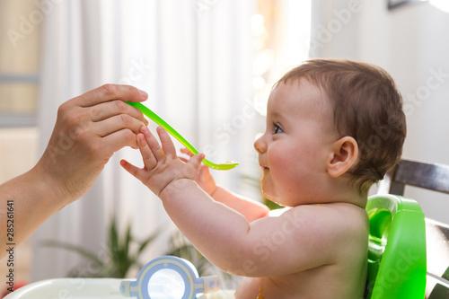 Adorable baby eating food. His mother feeds him with a spoon.