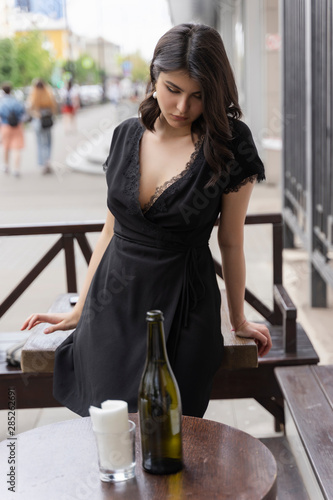 Beautiful elegant brunette girl wearing a black dress with a sexy deep neckline is relaxing in a street cafe. Advertising  fashion  commercial design. Copy space