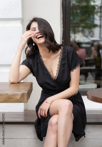 Photography Beautiful elegant brunette girl wearing a black dress with a sexy deep neckline is relaxing in a street cafe