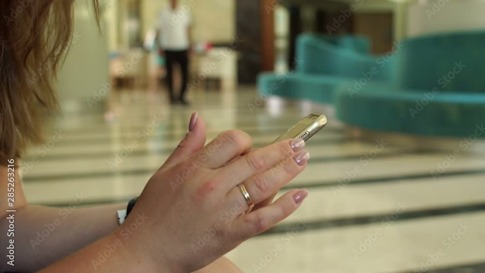 Close-up of a girl holding a phone sitting in the lobby of a hotel or cafe, a small child looks into the screen. Mom with phone in hand, the child looks at the screen. Slow motion. Close-up of a girl holding a phone sitting in the lobby of a hotel or cafe, a small child looks into the screen. Mom with phone in hand, the child looks at the screen. Slow motion.