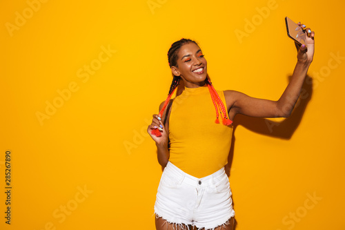 Image of happy african american woman with colorful braids smiling and taking selfie photo on smartphone © Drobot Dean