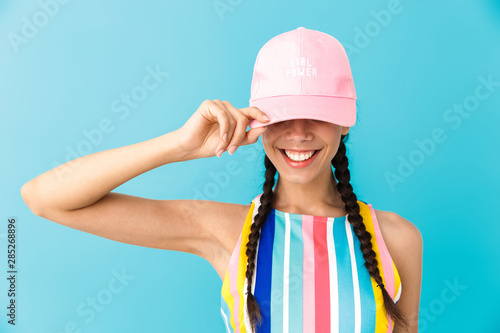 Image of stylish brunette girl wearing summer dress and cap smiling at camera