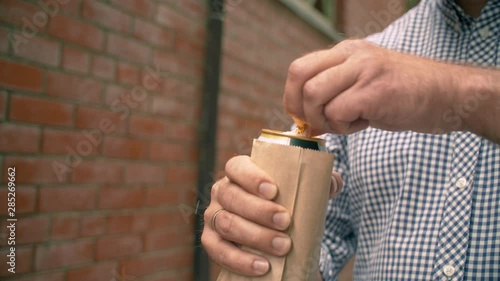 Brutal man illegally drinking beer. He put the beer can into a paper bag