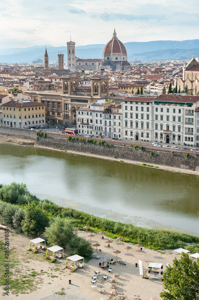 Sunbed and sunshades on the Arno river urban beach. Florence cityscape in a summer day.