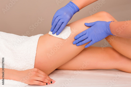 Beautician waxing female legs in spa center. Removing unnecessary hair on the legs. Procedure sugaring in a beauty salon. Sugar depilation. Depilatory sugar paste. Epilation with liquate sugar at legs
