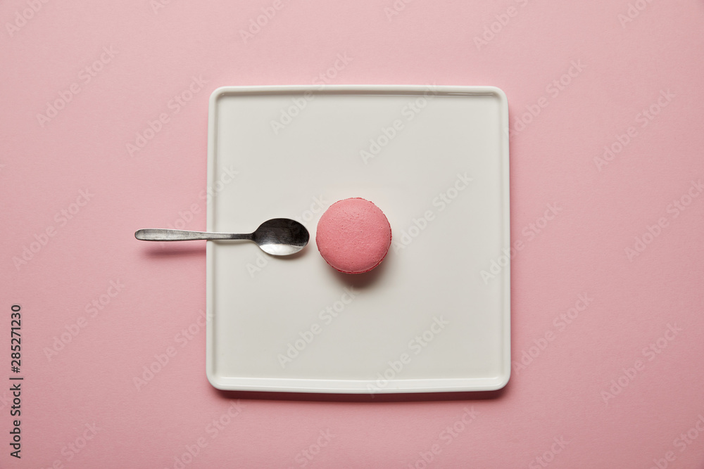 Top view on pink macaroon with teaspoon on white square dish on pink background Top view on pink macaroon with teaspoon on white square dish on pink background