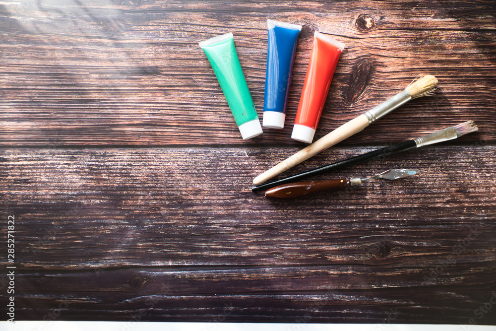 Obraz premium Red, green and blue paint tubes with paintbrushes in the wooden background