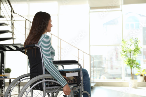 Young woman in wheelchair indoors. Space for text