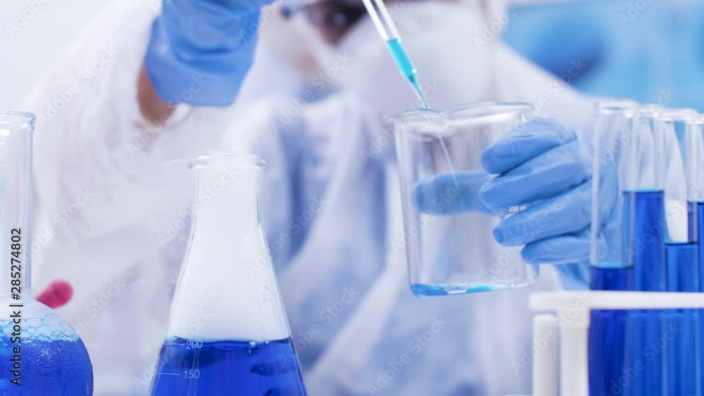 Close up of scientist taking multiple samples from a smoking blue fluid using a pipette. Scientist in protection equipment. Close up of scientist taking multiple samples from a smoking blue fluid using a pipette. Scientist in protection equipment.