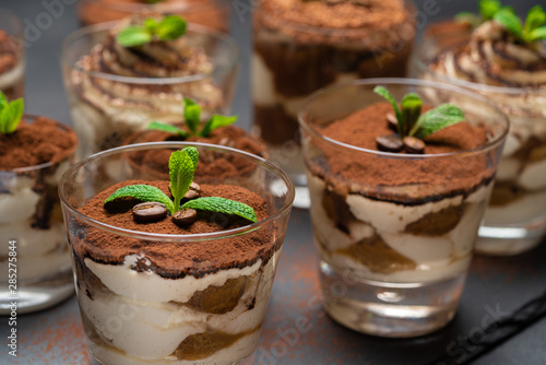 Group of portions of Classic tiramisu dessert in a glass cup on stone board on concrete background