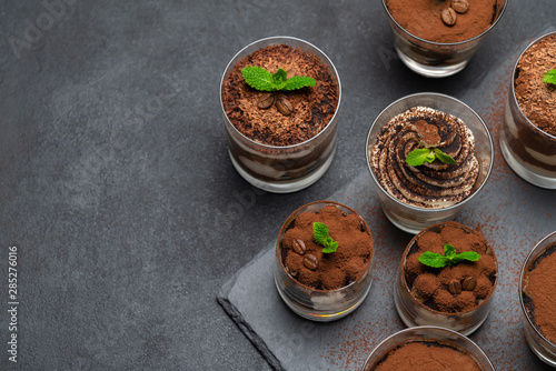 Group of portions of Classic tiramisu dessert in a glass cup on stone board on concrete background