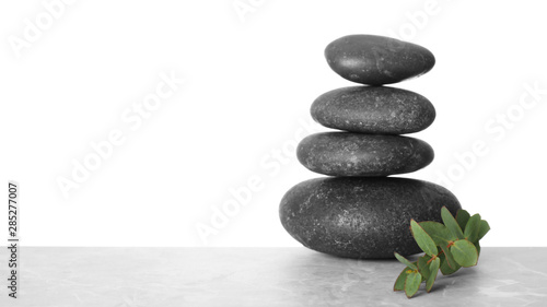 Stack of spa stones and green leaves on table against white background. Space for text