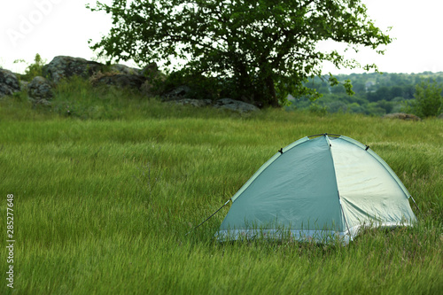 Modern camping tent in green field. Space for text